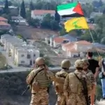 Tentara Lebanon berdiri di sebuah bukit menghadap Kota Metula di Israel ketika seorang pria mengibarkan bendera Palestina dan Hizbullah di Perbatasan Lebanon-Israel di Desa Selatan Kafr Kila, Lebanon, pada (9/10/2023) (Foto: Dok. Mohammed Zaatari/AP)