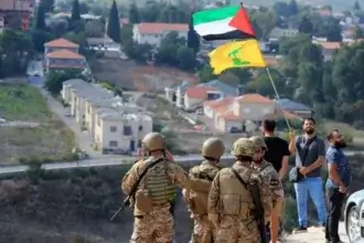 Tentara Lebanon berdiri di sebuah bukit menghadap Kota Metula di Israel ketika seorang pria mengibarkan bendera Palestina dan Hizbullah di Perbatasan Lebanon-Israel di Desa Selatan Kafr Kila, Lebanon, pada (9/10/2023) (Foto: Dok. Mohammed Zaatari/AP)